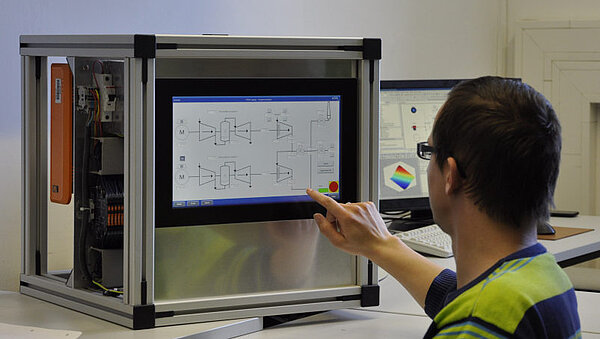 Person sitzt vor einem Monitor in einem Kasten und sieht digitales Schaltbild