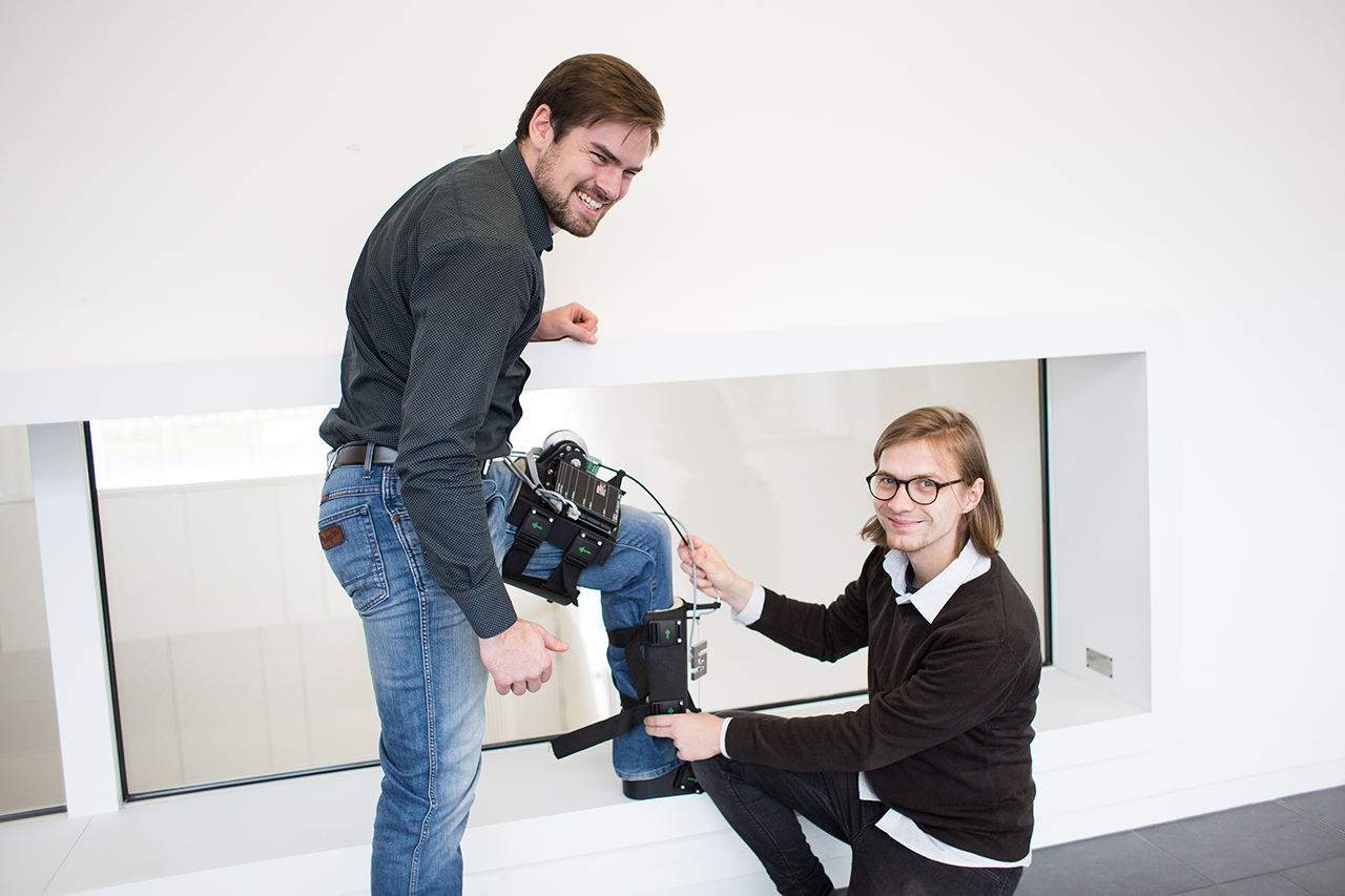 Präsentation des Exoskeletts: Mann hat Exoskelett am Bein und Bein ist erhöht, andere Wissenschaftler präsentiert Konstruktion/bei Verlinkung führt Link zur Projektwebsite