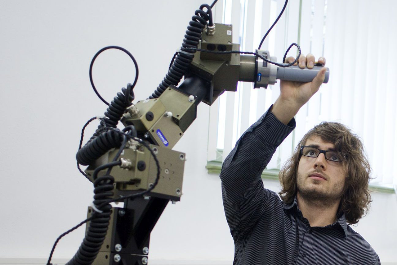 Wissenschaftler ergreift Arm an Industrierobotermodells/bei Verlinkung führt Link zur Projektwebsite
